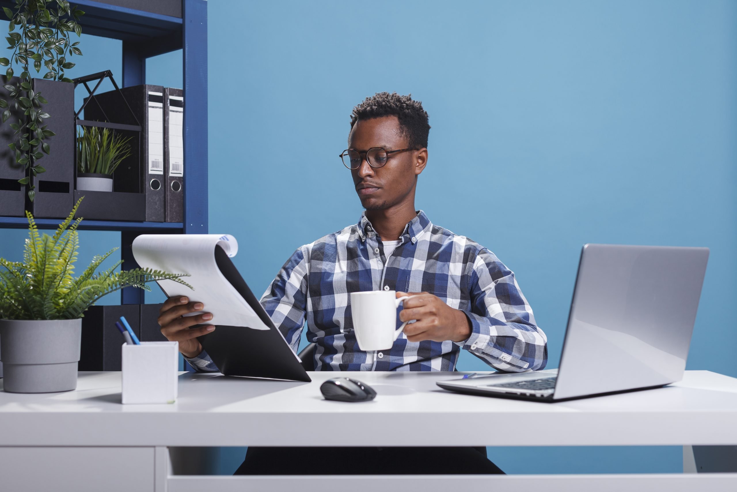 Young african american employee sitting in modern workspace while reviewing paperwork for real estate investment options.