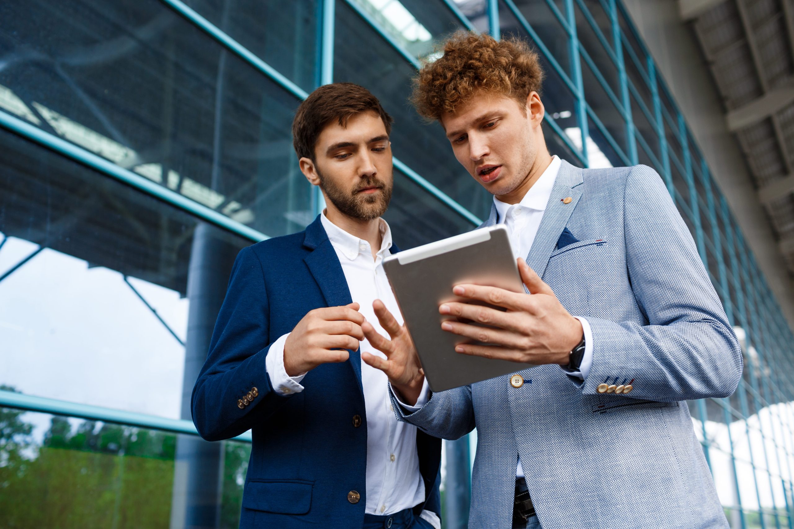 Two young investors talking on station about fixed income investments while holding tablet.
